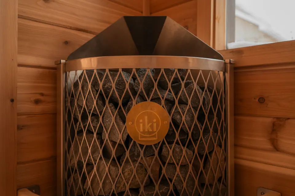 IKI sauna stove with its mesh basket full of stones in a cedar corner