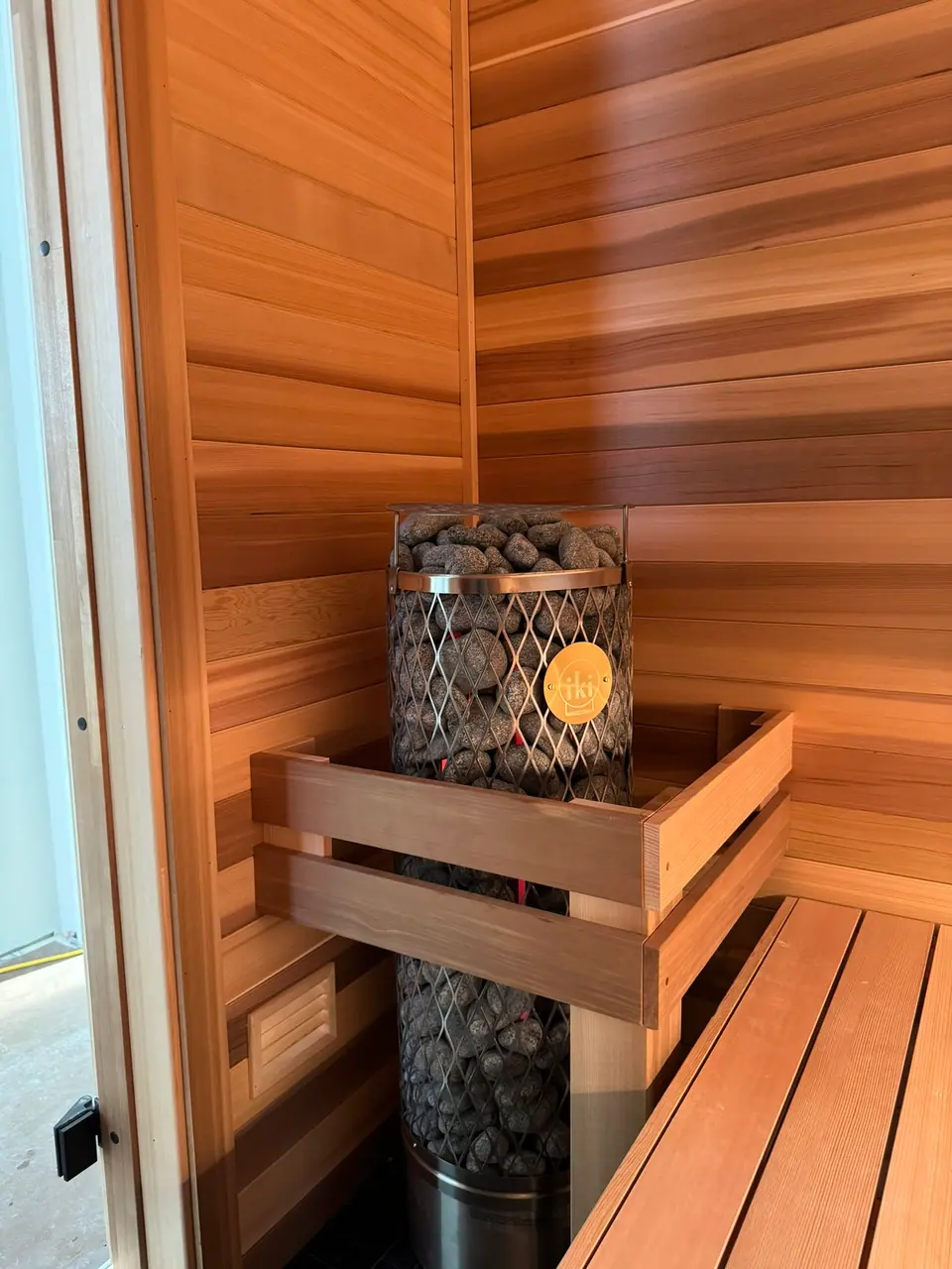 Electric sauna heater behind a cedar guard in an indoor sauna