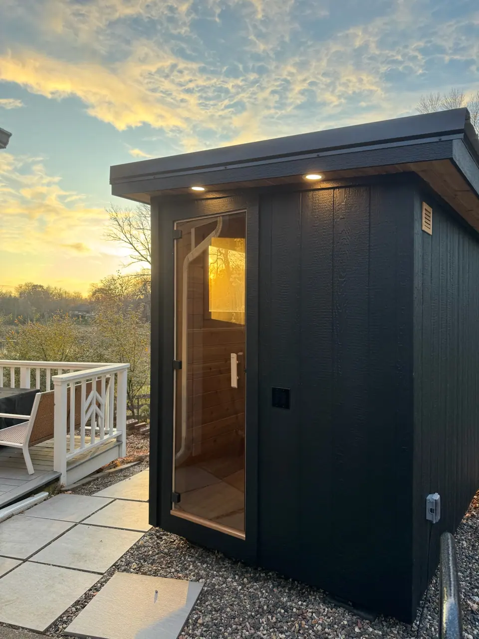 Compact black Kota sauna with a full-glass door at sunset