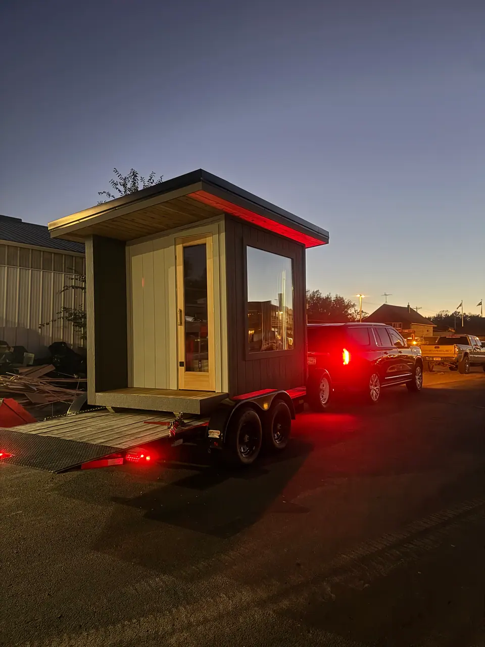 Finished sauna loaded on a trailer behind a truck at dusk, ready for delivery