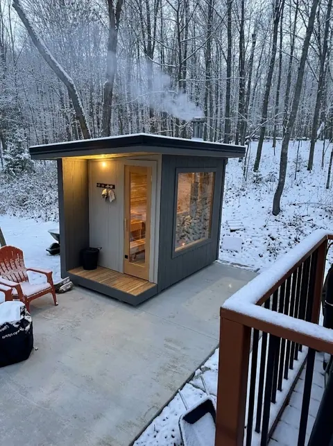 Sauna with a covered porch on a concrete patio in light snow