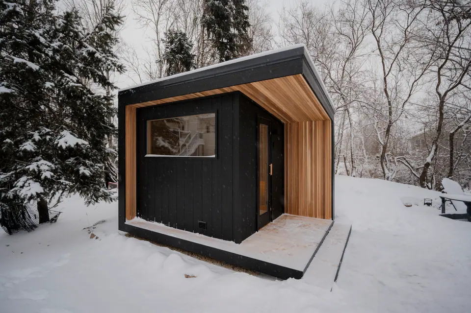 Black board-and-batten Tuli sauna with a clear cedar entry on a snowy day
