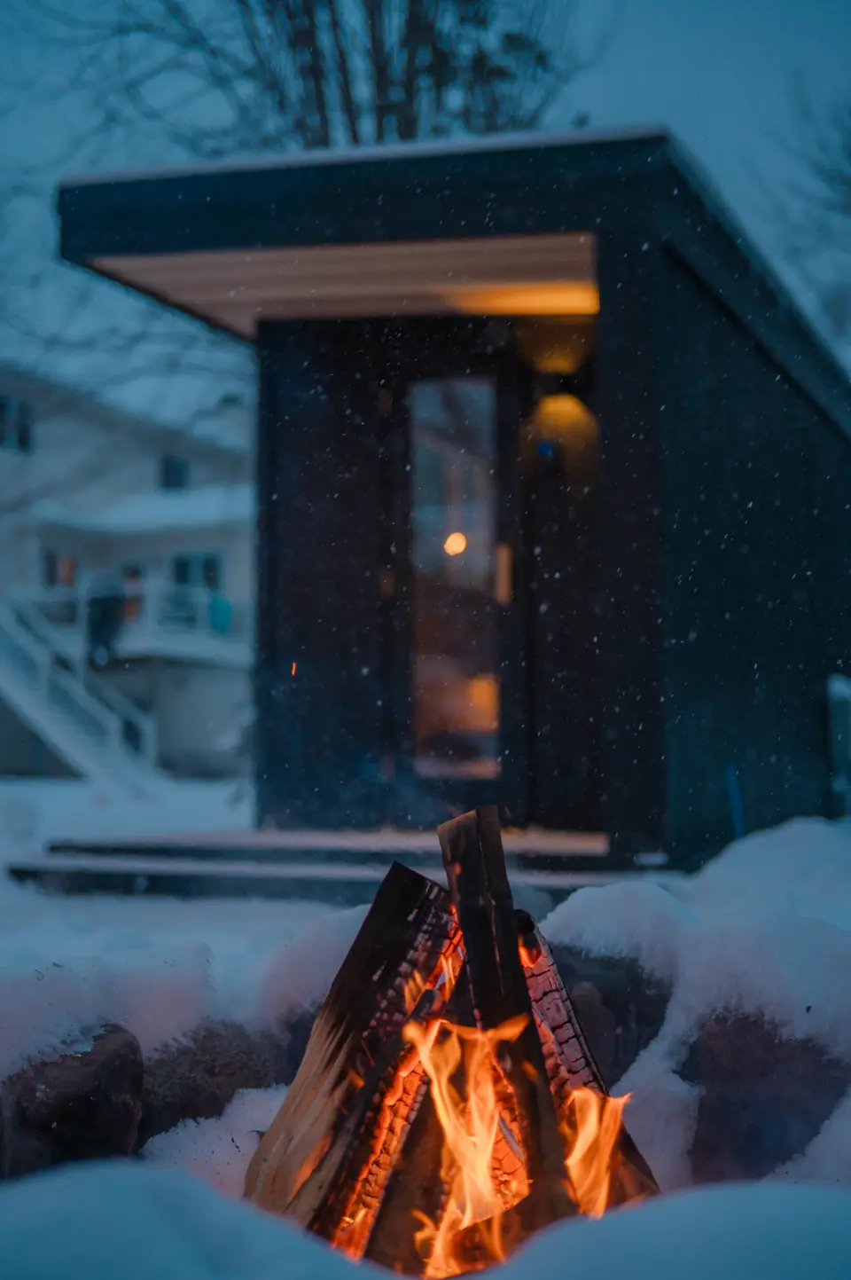 Fire pit burning in the snow with the Tuli sauna glowing behind it